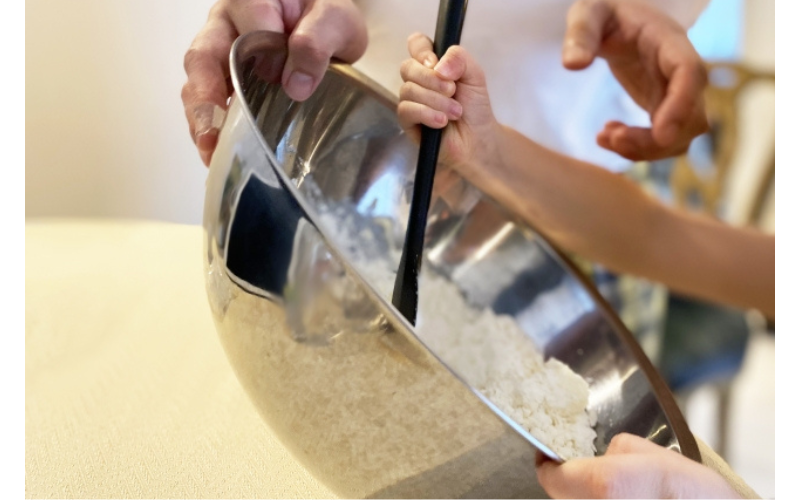 小さな手でボウルの粉を混ぜている2歳児の写真